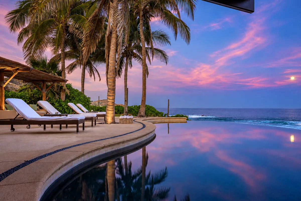 Palm trees beside an oceanfront infinity pool at dusk in Cabo San Lucas