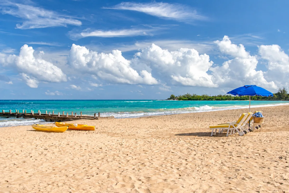 Yellow kayaks and loungers under a blue parasol on a sandy Jamaican beach