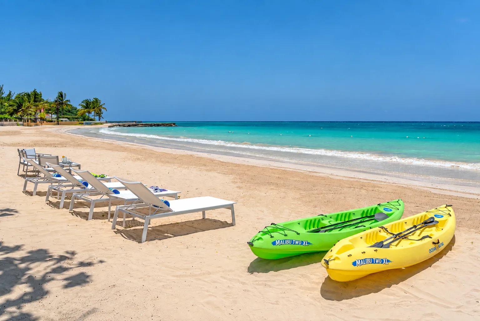 Green and yellow kayaks beside loungers on a turquoise-water beach in Jamaica