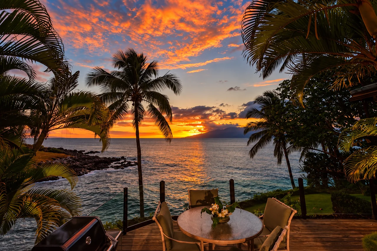 An oceanfront Maui dining terrace beneath palm trees at sunset