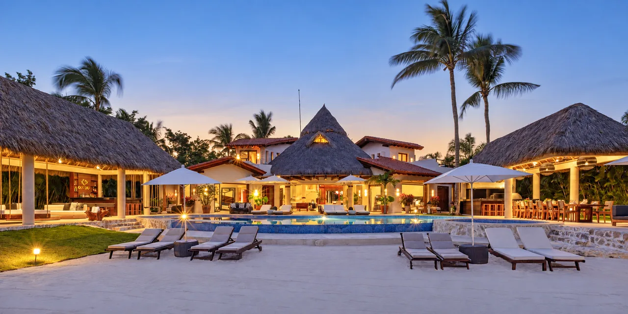 A beachfront villa with thatched pavilions and palm trees at dusk in Punta Mita