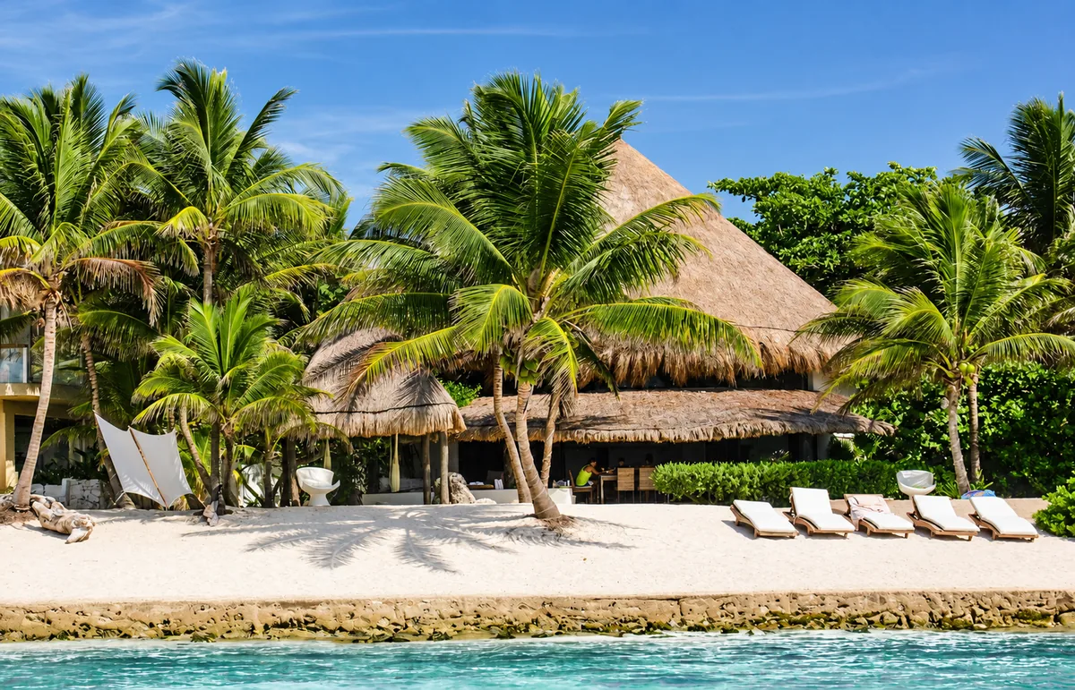 A thatched-roof beachfront villa and loungers among palms in Riviera Maya