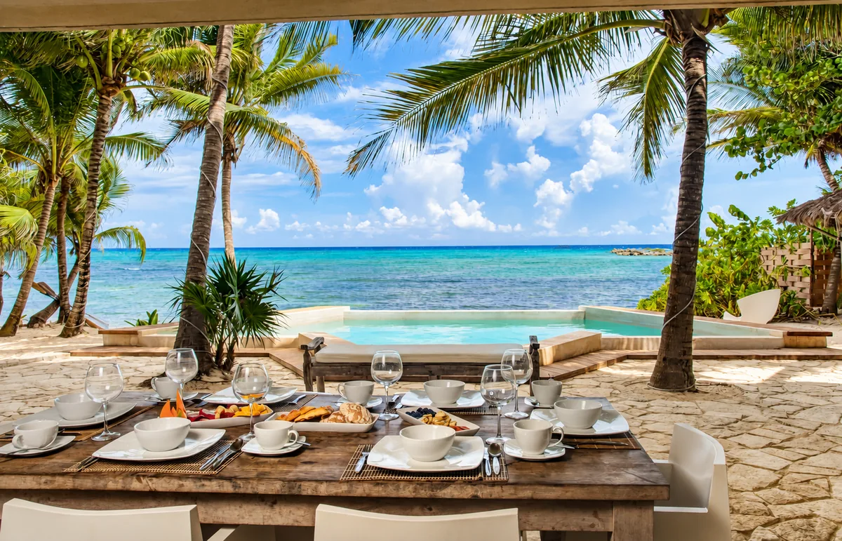 An outdoor breakfast table overlooking palms, a pool and the Caribbean in Riviera Maya