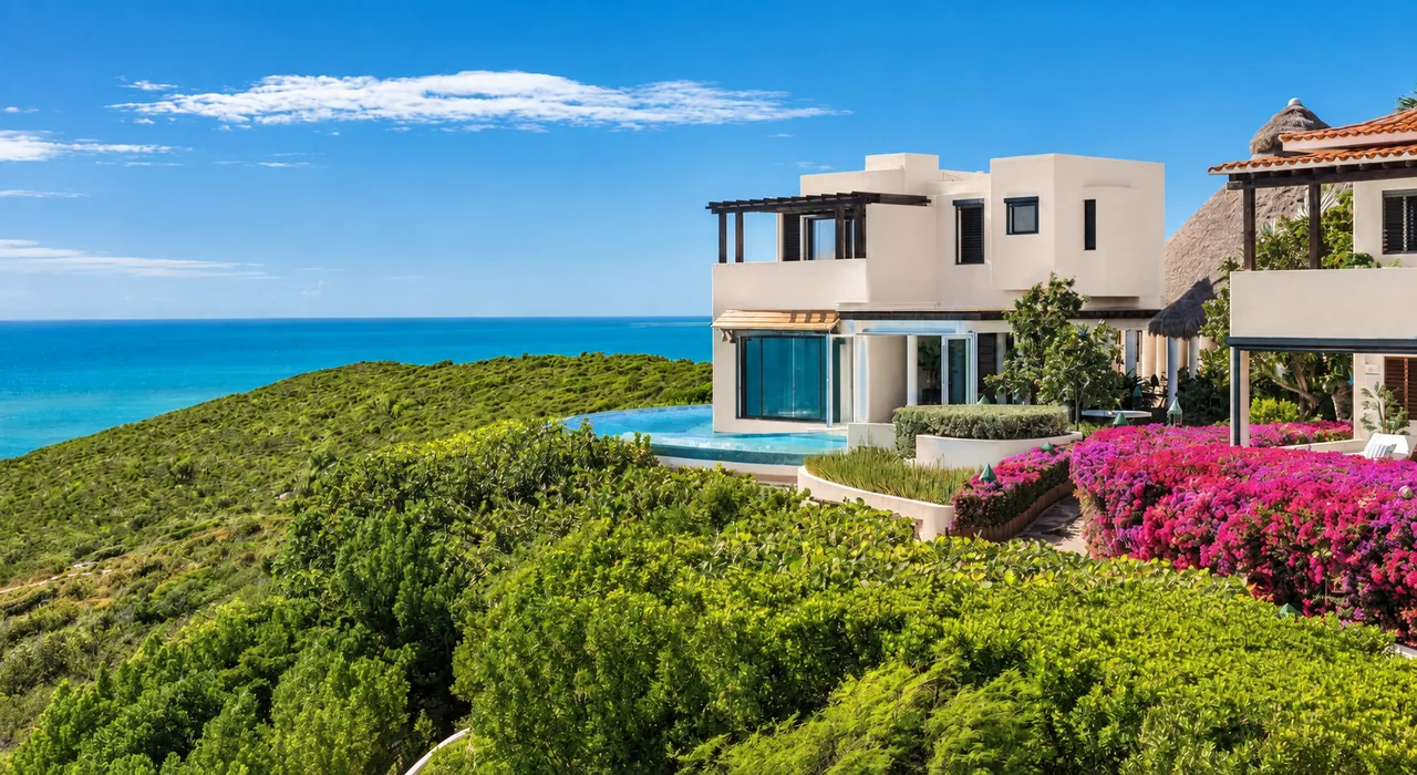 A coastal villa with an infinity pool and flowering gardens above turquoise water