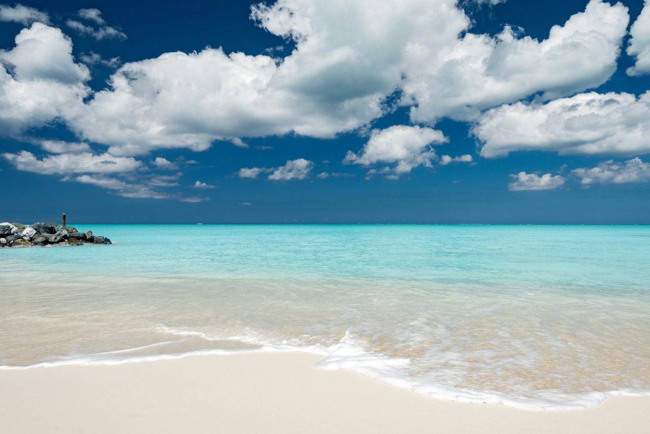 Pale sand and turquoise Caribbean water beneath a cloud-filled sky