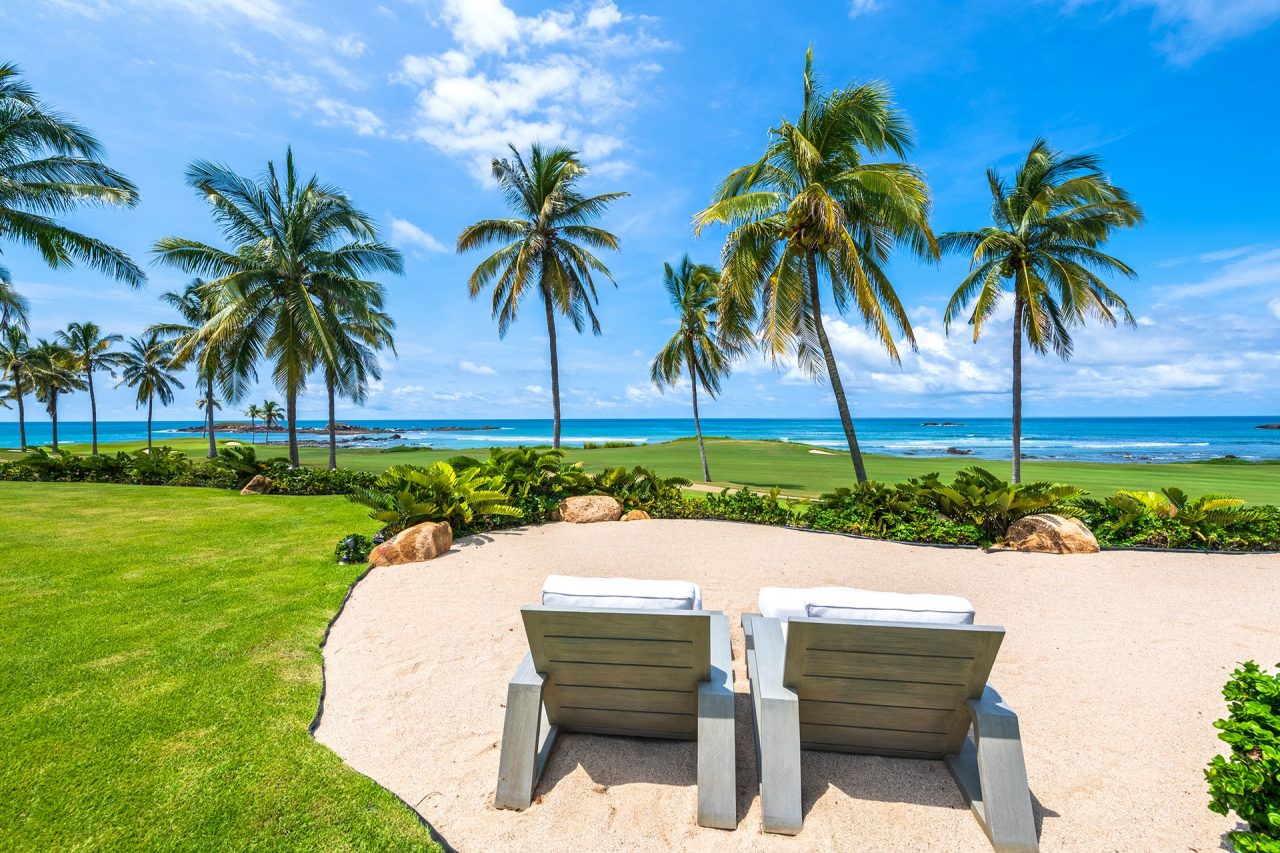 Two lounge chairs beneath palm trees overlooking the sea at a Mexico villa